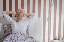 Una hermosa mujer mayor con cabello corto y gris en la cama en pijama por la mañana.