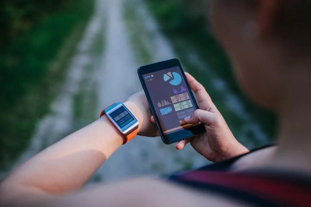 Mujer sincronizando su reloj inteligente y dispositivo móvil con los nuevos datos del entrenamiento.