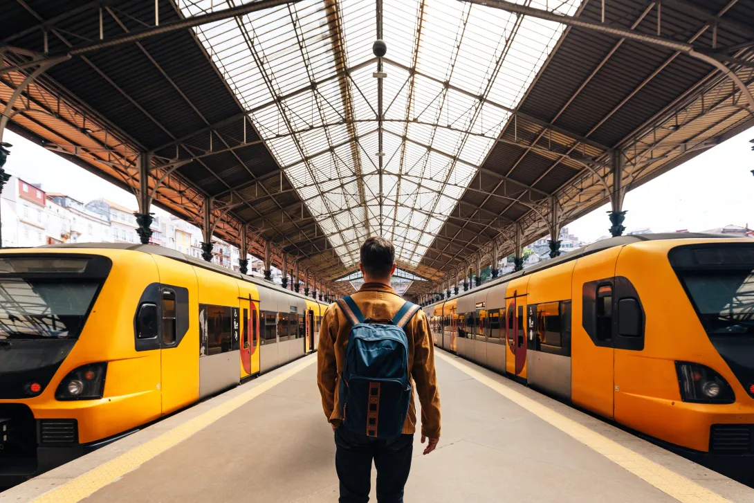 Turista con mochila caminando entre trenes en la estación de tren